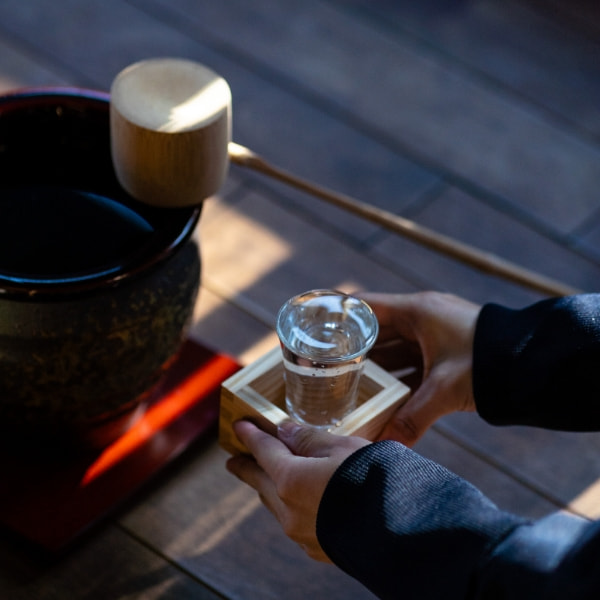 黒い酒器と、枡に載せたグラスの日本酒を差し出す手