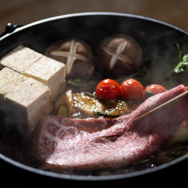 湯気の立つすき焼き鍋。和牛、焼き豆腐、椎茸、ミニトマト