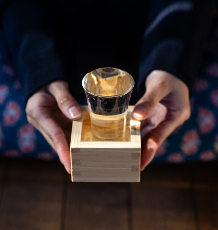 枡に載せたグラスの搾りたて日本酒を両手で差し出す