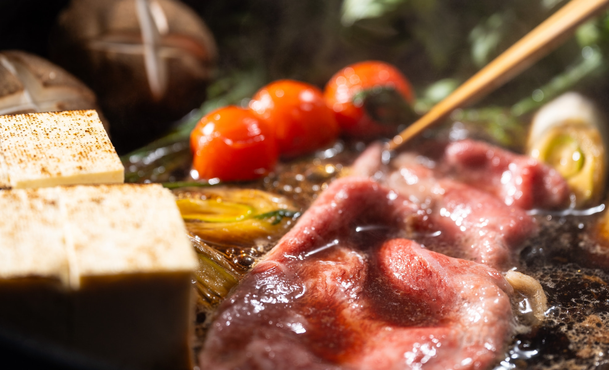 煮立つ割下のなかの和牛スライスと焼き豆腐、ミニトマト
